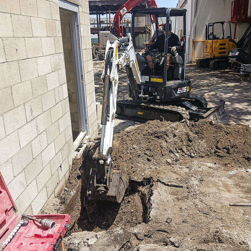 Compact excavator digs trench for underground sanitary piping.