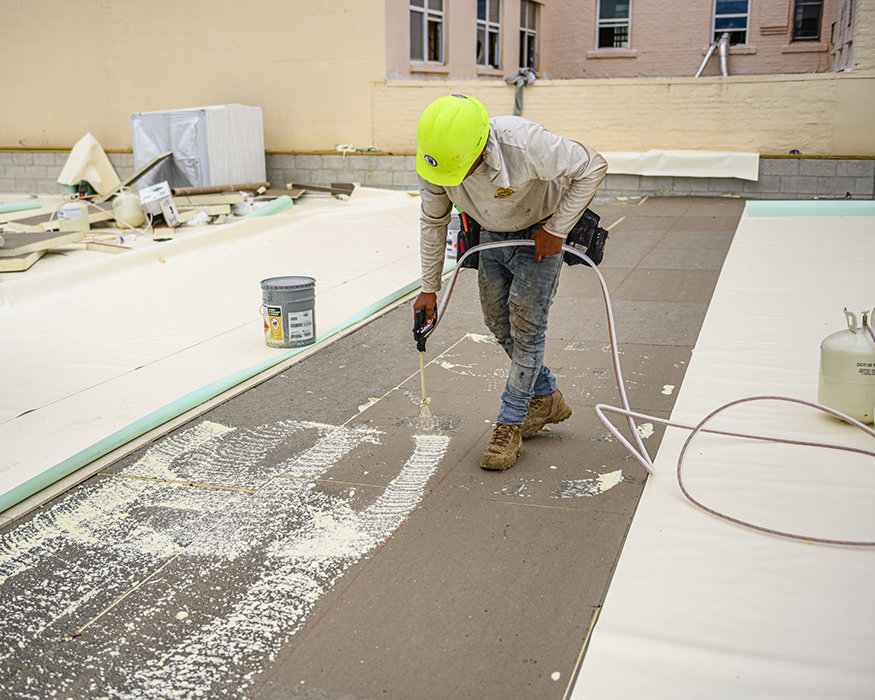 Worker applies adhesive beneath roof insulation boards.