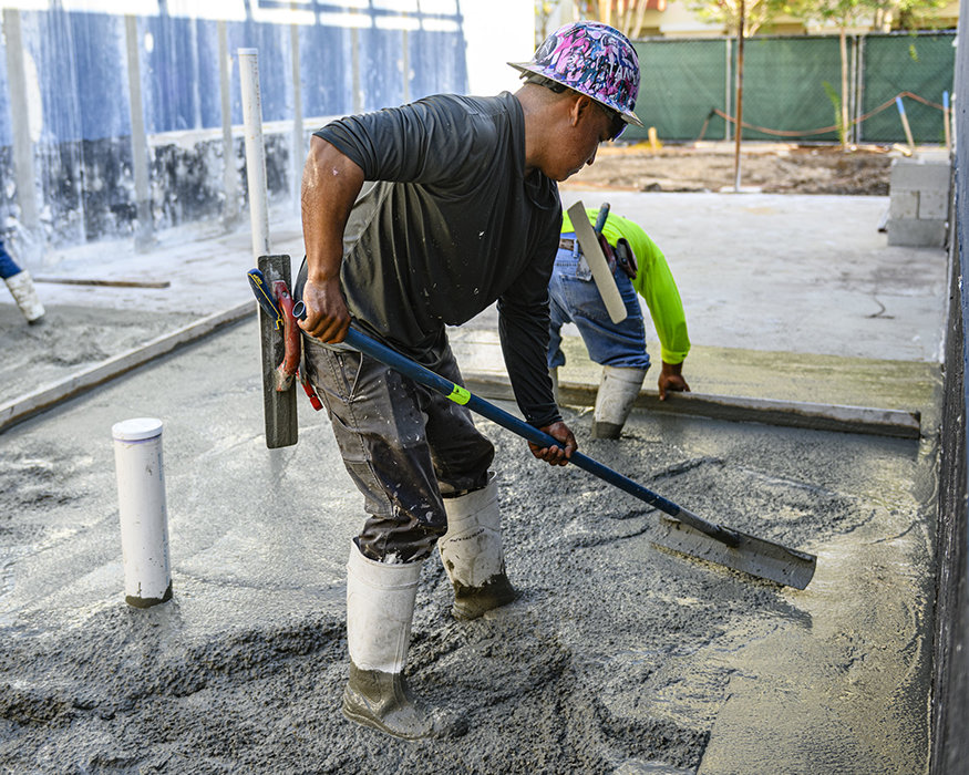 Worker levels fresh concrete across interior floor.