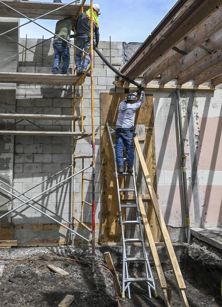 Workers pump grout into front CMU wall cells.