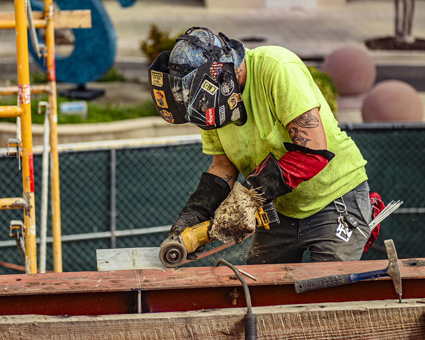 Worker uses angle grinder to prepare steel bracket.