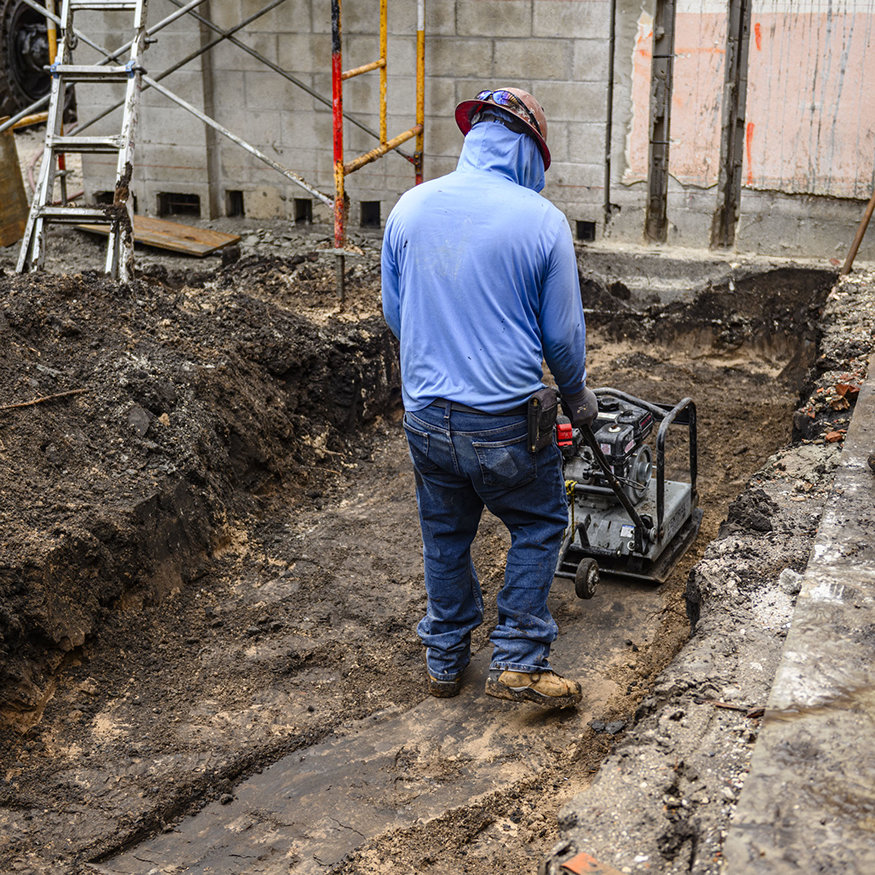Worker compacts soil inside foundation excavation.