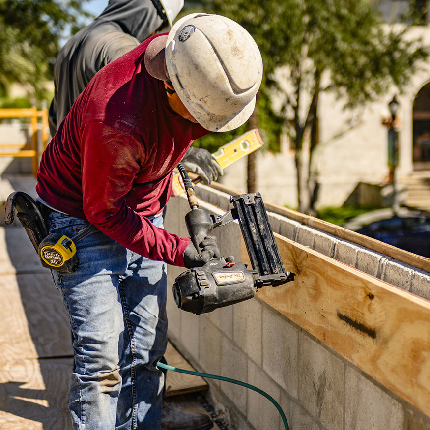 Worker secures parapet formwork with nail gun.