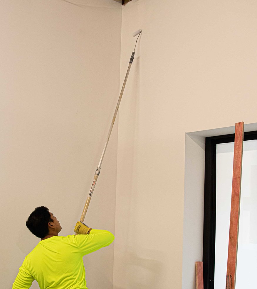 Worker rolls paint near exposed ceiling beams. 