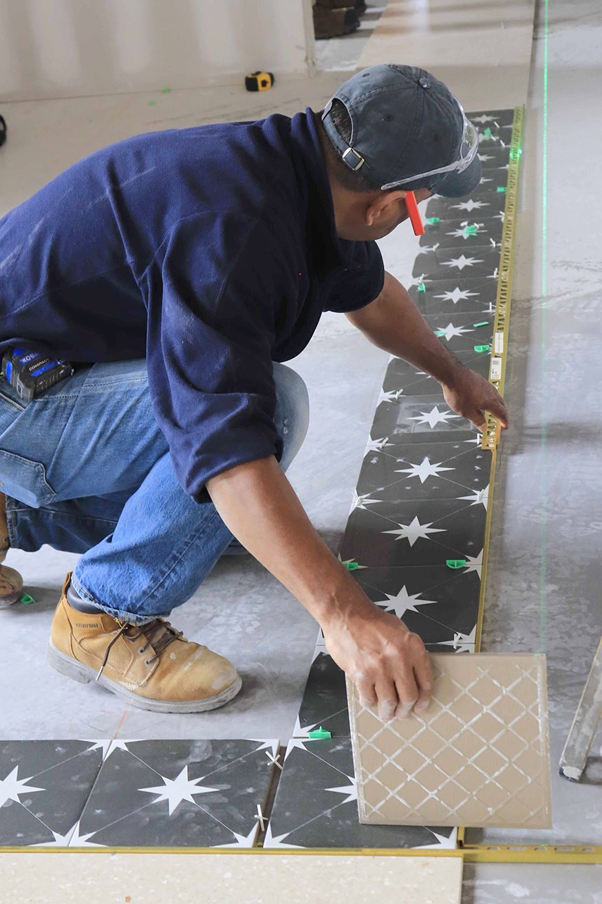 A leveling laser is used to confirm accurate tile placement.