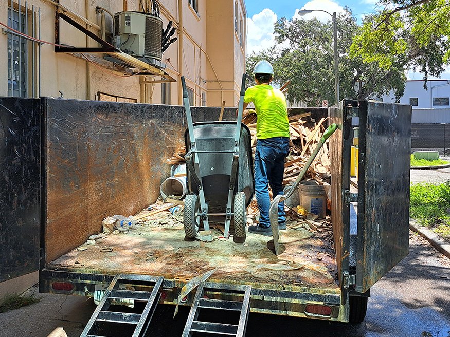 Worker loads wall debris from interior demo into trailer behind Brown Brothers building.