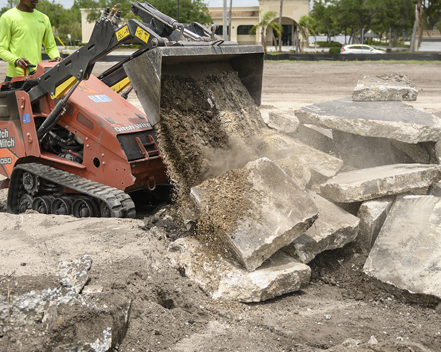 Loader dumps soil and debris onto removed concrete slabs.