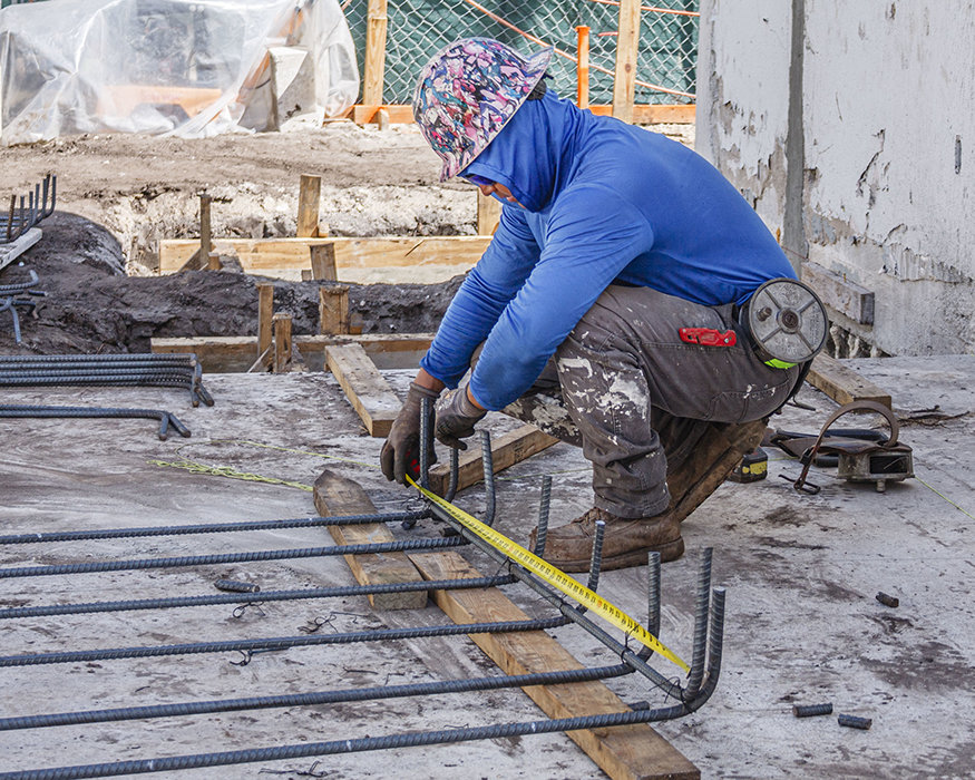 Worker measures reinforcing bar for footing cage.