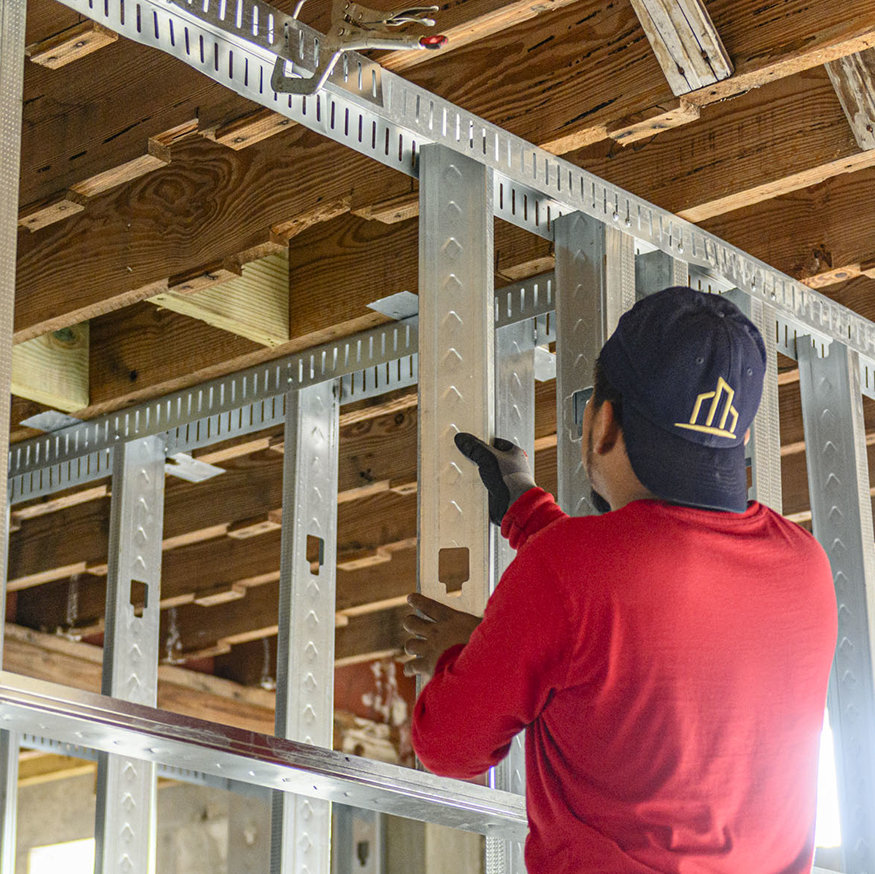 Worker positions vertical metal stud in interior framing.