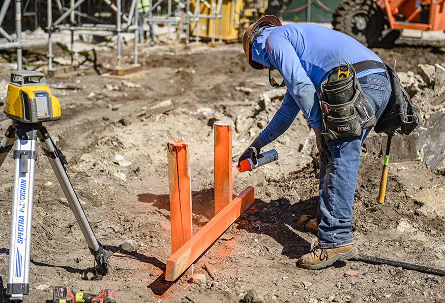 A worker marks the planned foundation and wall locations with orange paint.