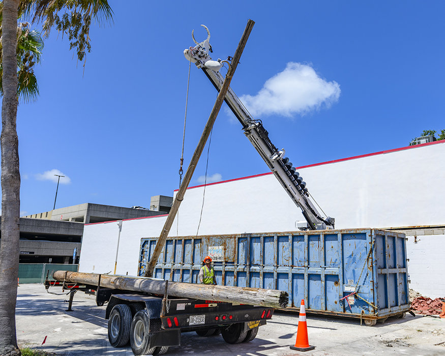 Contractors use a bucket truck to lower a removed utility pole onto a trailer.